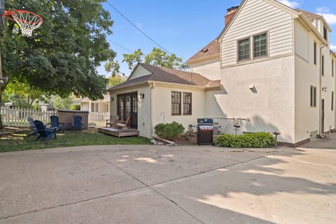 Exterior view of a charming property showcasing a backyard with seating, BBQ grill, basketball hoop, and ample parking.
