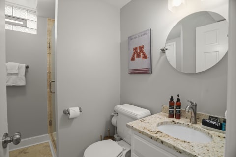 Interior of a modern bathroom with granite countertops, a round mirror, and a decorative collegiate wall hanging.