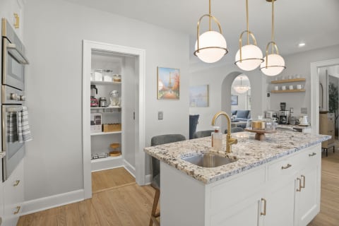 A modern kitchen featuring granite countertops, pendant lighting, and a walk-in pantry, with a seamless connection to the living area.