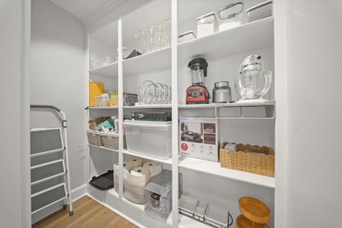 A bright and organized pantry with shelves filled with kitchen appliances, storage containers, and cooking tools.