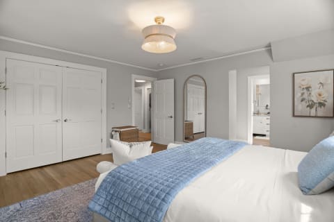 A calming bedroom with gray walls, warm wooden floor, and a bed dressed in blue accents.