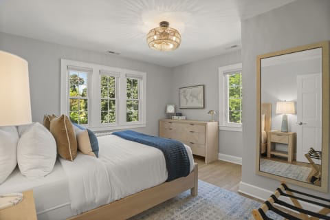 A bright and tranquil bedroom featuring a cozy bed, multiple windows, and stylish furniture.