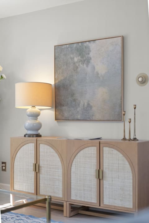 A stylish console with woven-front cabinets, a warm lamp, and an abstract painting on the wall, creating a welcoming entryway space.