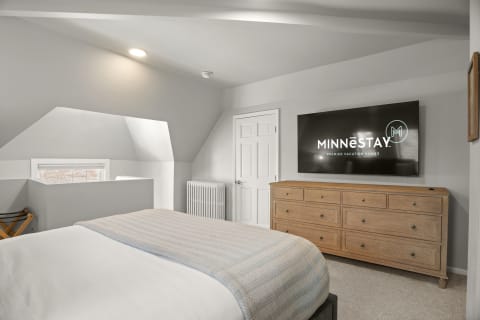 Inviting bedroom featuring a plush bed, wooden dresser, and mounted TV, showcasing a peaceful, modern retreat.