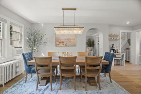 A beautifully decorated dining room with a chandelier, wooden dining table, blue chairs, and a serene painting.