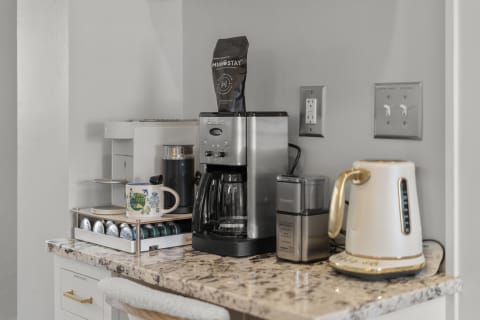 A coffee station with a coffee maker, kettle, and colorful coffee pods on a countertop.