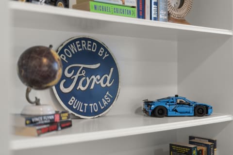 A white bookshelf with a blue Ford sign, a globe, and a blue model car with books arranged neatly.