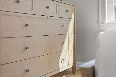 Light wood dresser with black knobs illuminated by sunlight.
