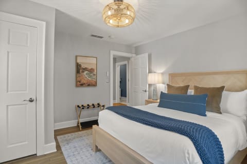 A cozy bedroom featuring a queen-sized bed, soft linens, and warm lighting with a coastal art piece on the wall.