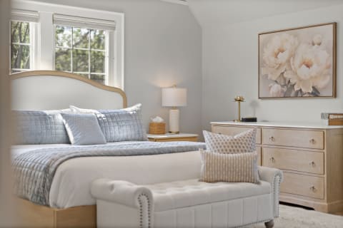A tranquil bedroom featuring a plush bed with blue-gray bedding, a stylish lamp, and an elegant floral painting on the wall.
