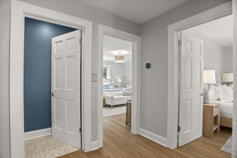 A hallway between two bedrooms featuring gray walls, a blue accent wall, and warm wooden flooring.