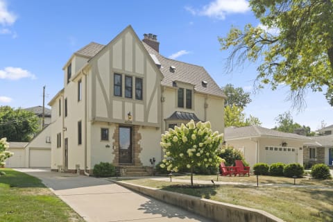 A Tudor Revival home with a decorative exterior and hydrangea tree in the yard.