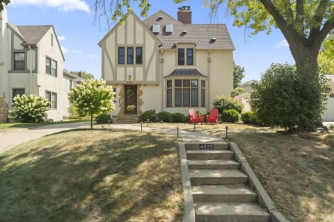 A Tudor-style home with a welcoming front lawn and red Adirondack chairs on the pathway.