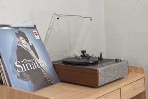 A turntable with a Sinatra vinyl album on a wooden console in a cozy setting.