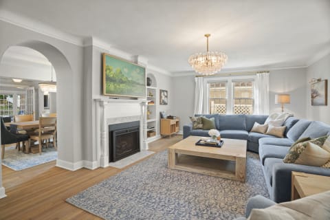 Cozy living room featuring a sectional couch, fireplace, and crystal chandelier with natural light from large windows.