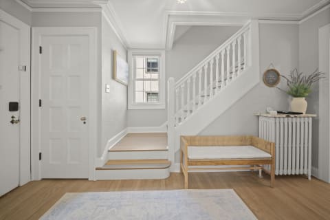 An airy entryway with a staircase, woven bench, and soft gray walls creating a warm atmosphere.