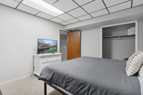 Modern bedroom with a gray bed, white dresser with TV, and an open closet.