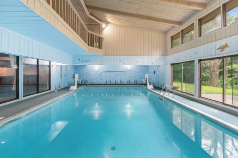 Indoor swimming pool surrounded by windows and blue-themed decor.