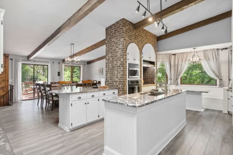 Modern kitchen featuring white cabinetry, granite countertops, and exposed wooden beams.