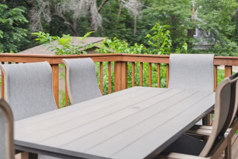 Outdoor dining setup featuring a wooden table and gray chairs on a deck amidst trees.