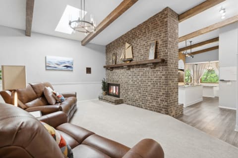 Living room with brown leather couches, a brick fireplace, and a modern chandelier.