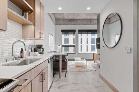A contemporary kitchen and living space in an apartment with wooden cabinets and large windows.