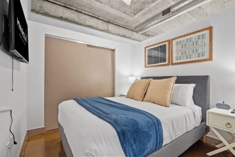 Modern bedroom with a gray upholstered bed, decorative pillows, and framed artwork on the wall.