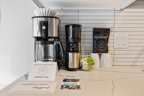 A modern coffee station featuring two coffee makers, coffee bags, and mugs.