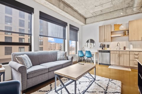 Modern living space featuring a gray sofa, coffee table, and kitchen area with blue chairs.