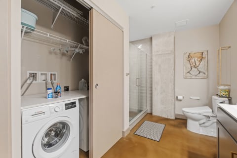 Contemporary bathroom featuring a washing machine, glass shower, and white toilet.