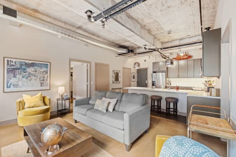 A contemporary living room featuring a gray sofa, yellow armchair, and a sleek kitchen.