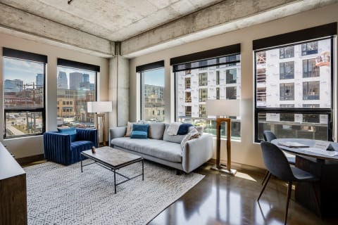 A modern living room featuring a gray sofa, blue armchair, and large windows with city views.