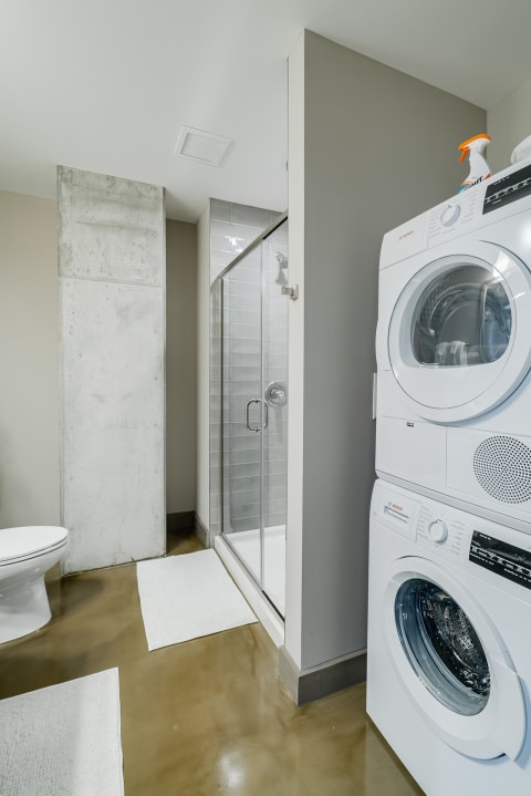 Modern bathroom with shower, toilet, and stacked washer-dryer unit.