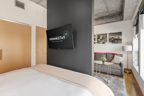 Modern interior showcasing a bedroom with a flat-screen TV, gray sofa, and cityscape wall art.