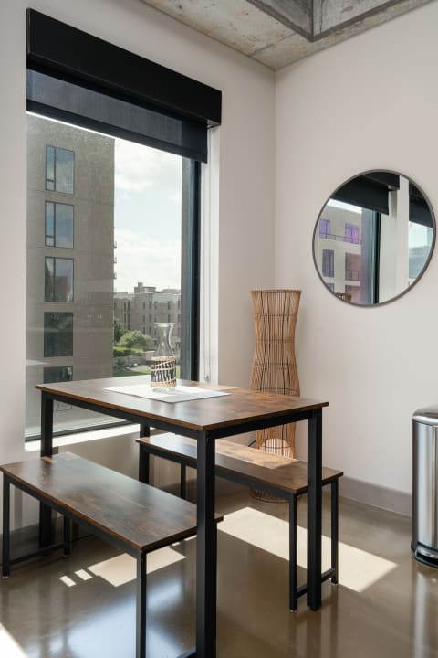 Contemporary dining area featuring a wooden table, benches, and large windows with a circular mirror.
