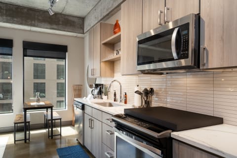 Modern kitchen featuring light wood cabinets, stainless steel appliances, and a small dining area by the window.
