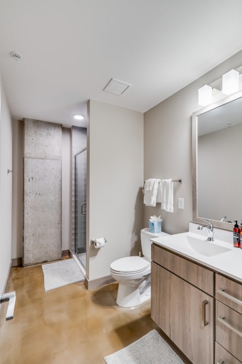 A modern bathroom featuring a white vanity, glass shower, and polished concrete floor.