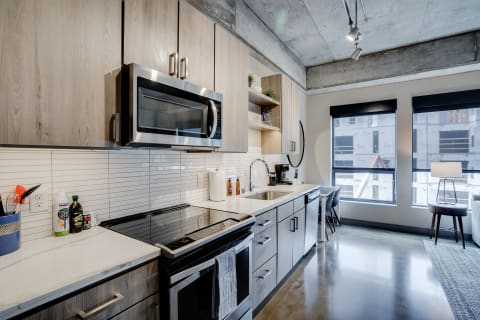 Modern kitchen with light wood cabinetry, stainless steel appliances, and large windows.