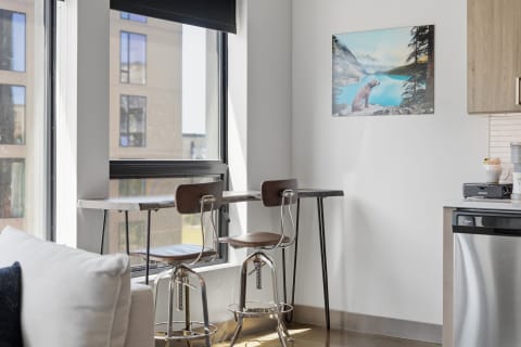 Dining nook with wooden bar stools, a marble table, and a landscape painting in a modern apartment.