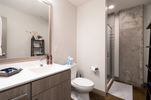 Modern bathroom featuring a vanity, toilet, and glass shower with concrete wall.