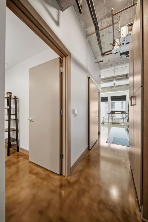 Modern hallway with polished concrete floors and high ceilings, featuring exposed beams and doors leading to other rooms.