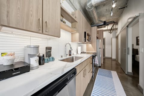 A modern kitchen with light wood cabinetry, marble countertops, stainless steel appliances, and a coffee station.