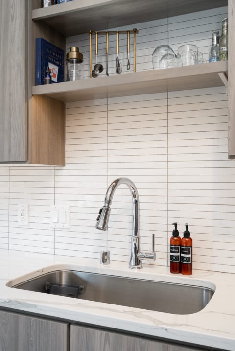 Modern kitchen sink with chrome faucet and wooden shelves storing kitchen items.