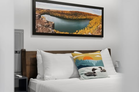 Cozy bedroom with a wooden headboard, crisp white linens, a nature-themed pillow, and a framed lake view artwork.