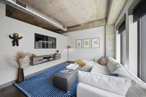 A modern living room featuring a plush sofa, blue striped rug, and a wall-mounted TV, illuminated by natural light.
