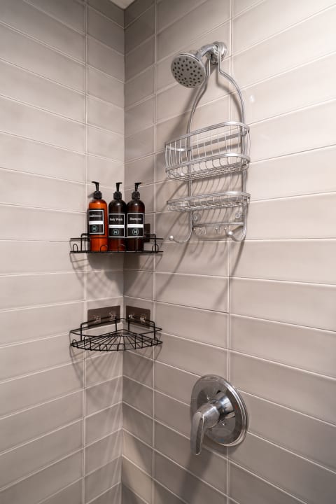 Contemporary shower corner with grey tiles, a showerhead, and storage for shampoo and body wash.