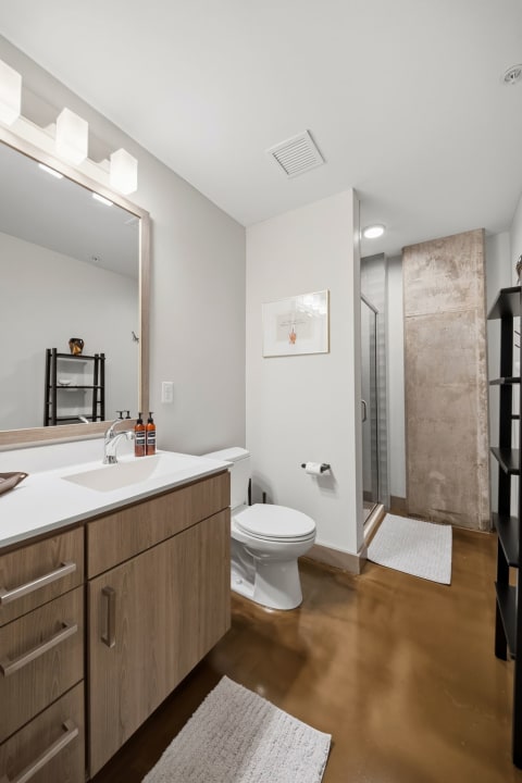 A modern bathroom featuring polished concrete finishes, a walk-in shower, and natural light.