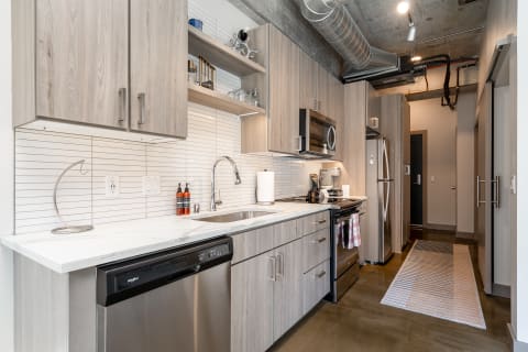 Modern kitchen with light wood cabinets, stainless steel appliances, and marble countertop.