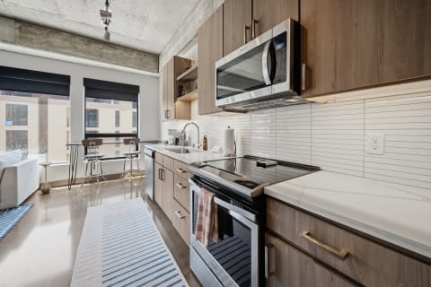 Modern kitchen with stainless steel appliances, wood cabinetry, and white marble countertops.