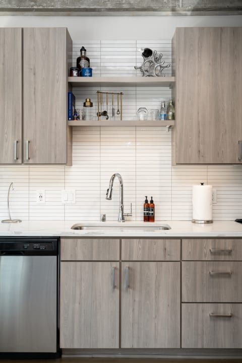 Modern kitchen featuring light wood cabinets, open shelves, and a stainless steel sink.